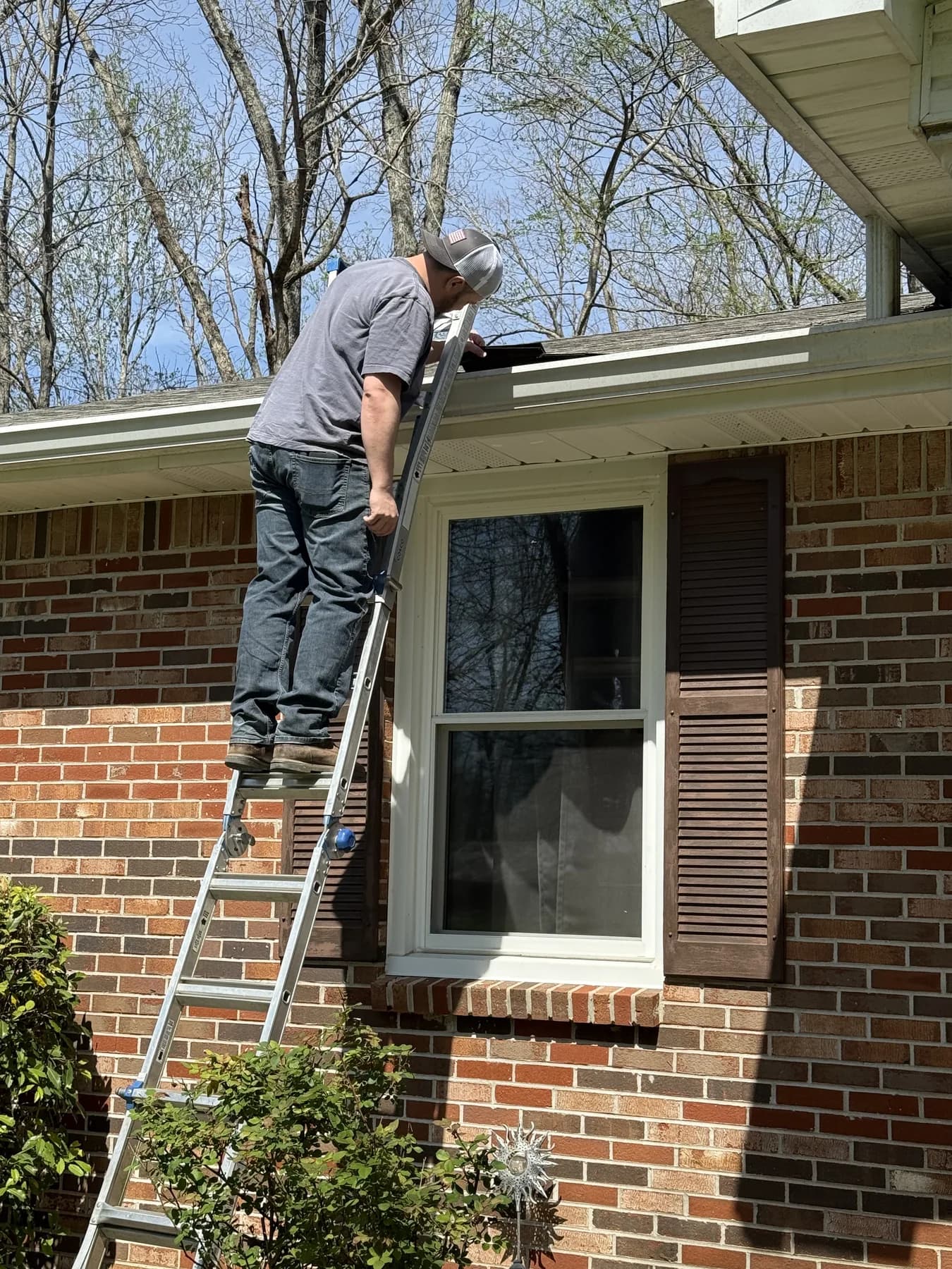 Worker inspecting or repairing an eave area on a brick home